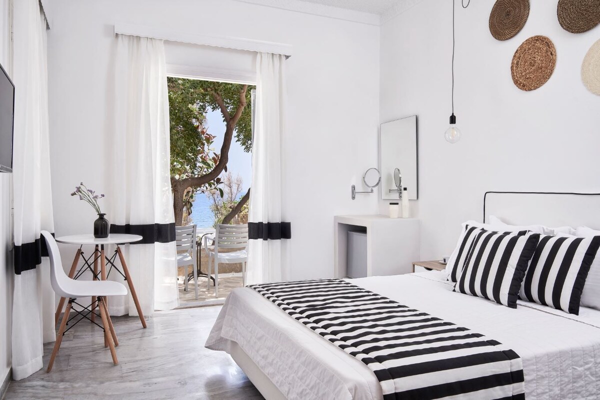 A modern hotel room with a bed, a desk, and a view of the sea.