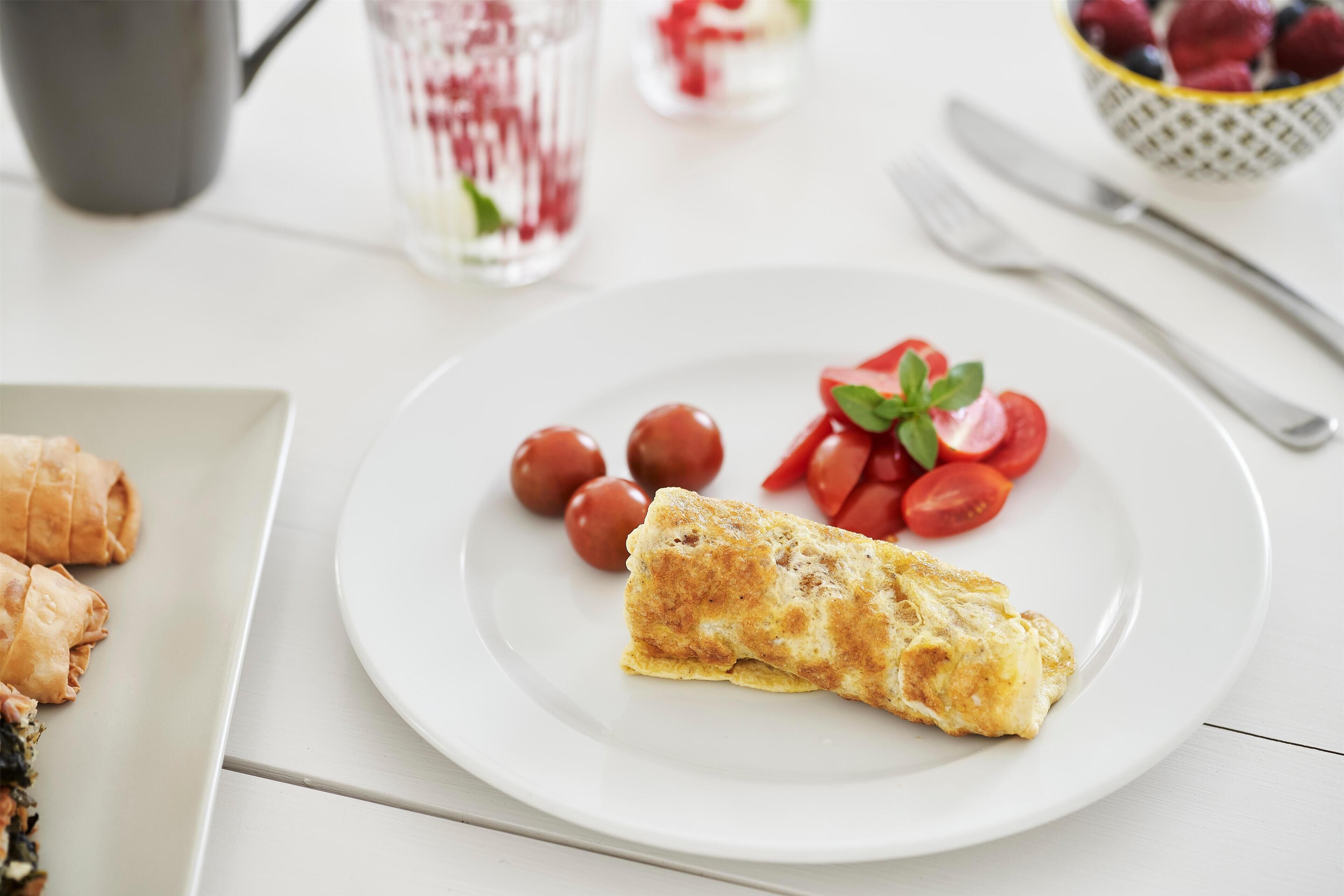 Un plato con una tortilla, tomates cherry y hojas de albahaca.