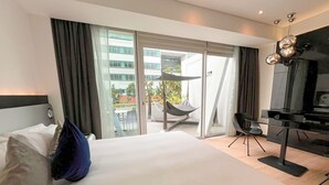 Een moderne hotelkamer met een groot bed, een bureau en een stoel. Er is een balkon met een hangmat en uitzicht op de stad.