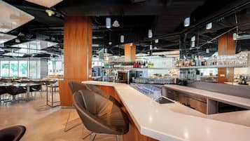 A modern bar area with a long counter, bar stools, and a variety of bottles and glasses.