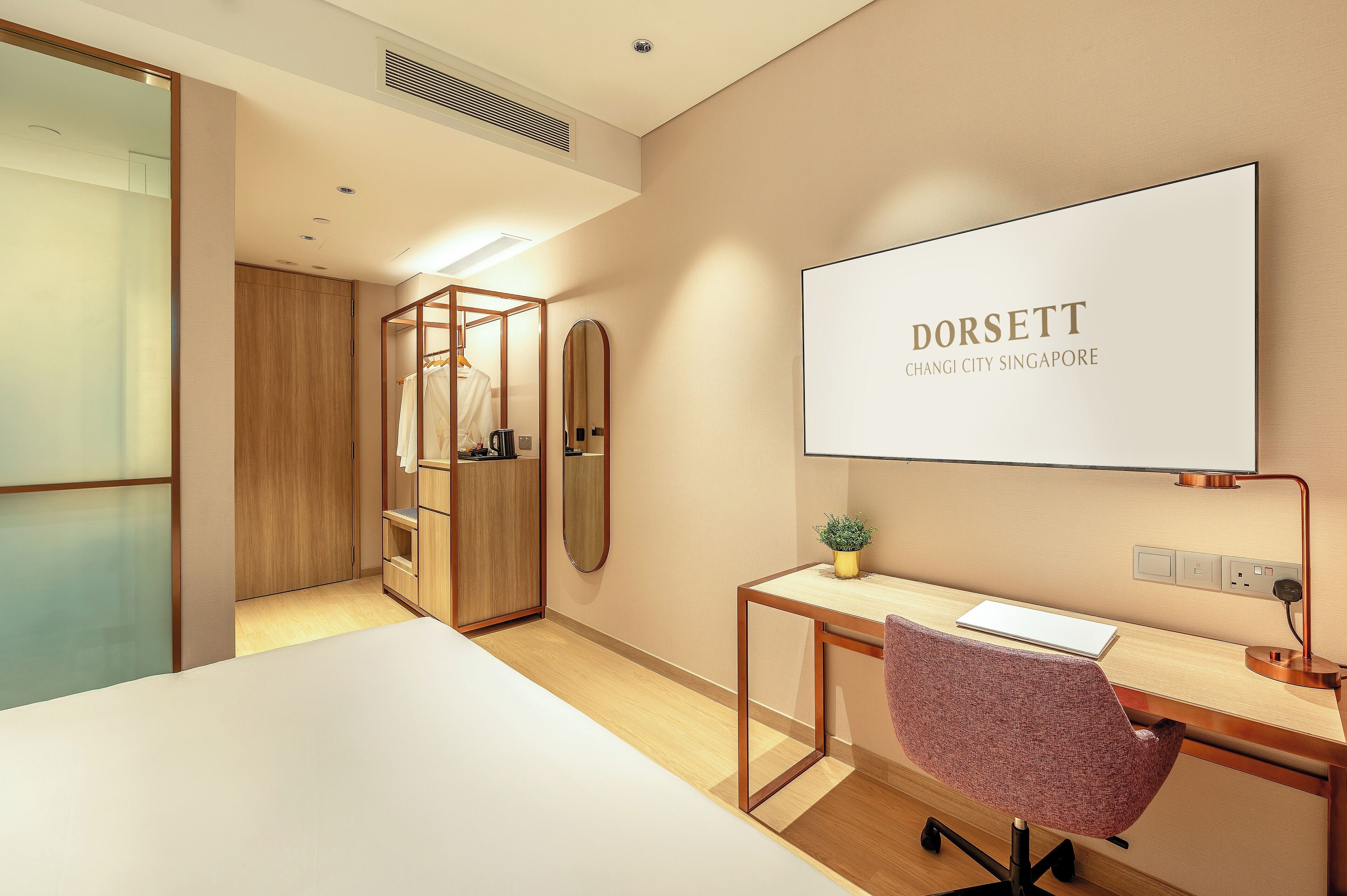 A modern hotel room with a large bed, a desk with a chair, a mirror, and a large window.