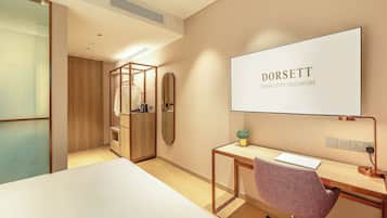 A modern hotel room with a large bed, a desk with a chair, a mirror, and a large window.