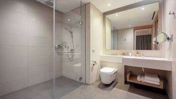 Un baño moderno con ducha envuelta en vidrio, inodoro blanco, lavabo con espejo y estante de madera con toallas.