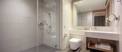 A modern bathroom with a glass-enclosed shower, a white toilet, a sink with a mirror, and a wooden shelf with towels.