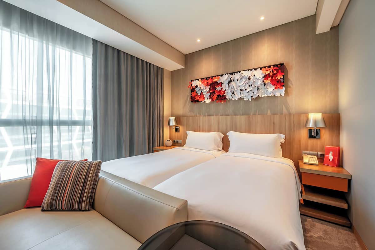 Una habitación de hotel con una cama grande, dos mesitas de noche, un sofá y un adorno en la pared.