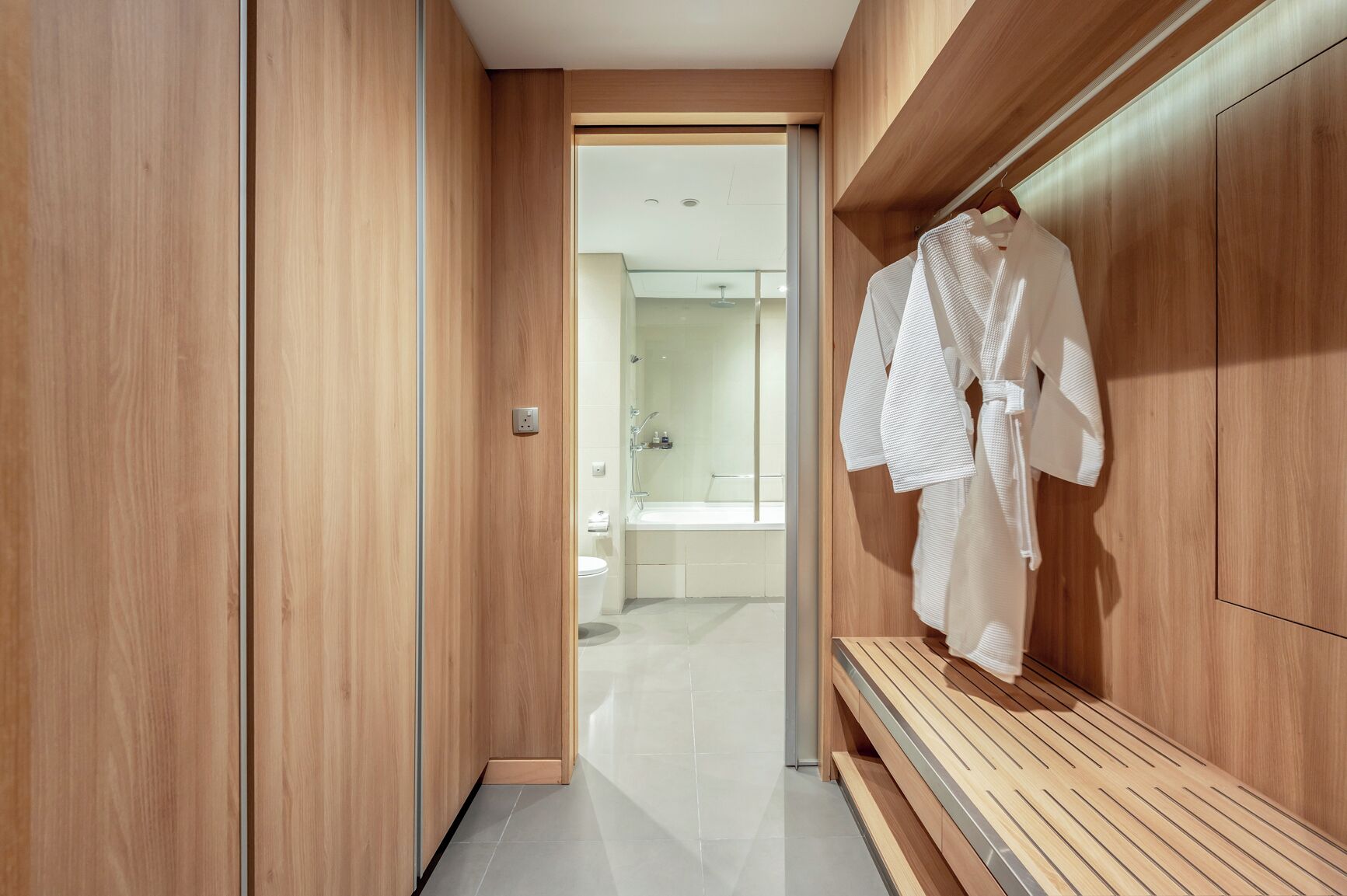 A modern bathroom with wooden cabinetry, a shower area, and a bench.