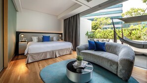 Een moderne hotelkamer met een groot bed, een bank, een salontafel en uitzicht op groen en een gebouw.