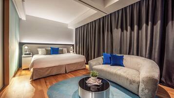 A modern hotel room with a large bed, a sofa, a coffee table, and a large window with curtains.