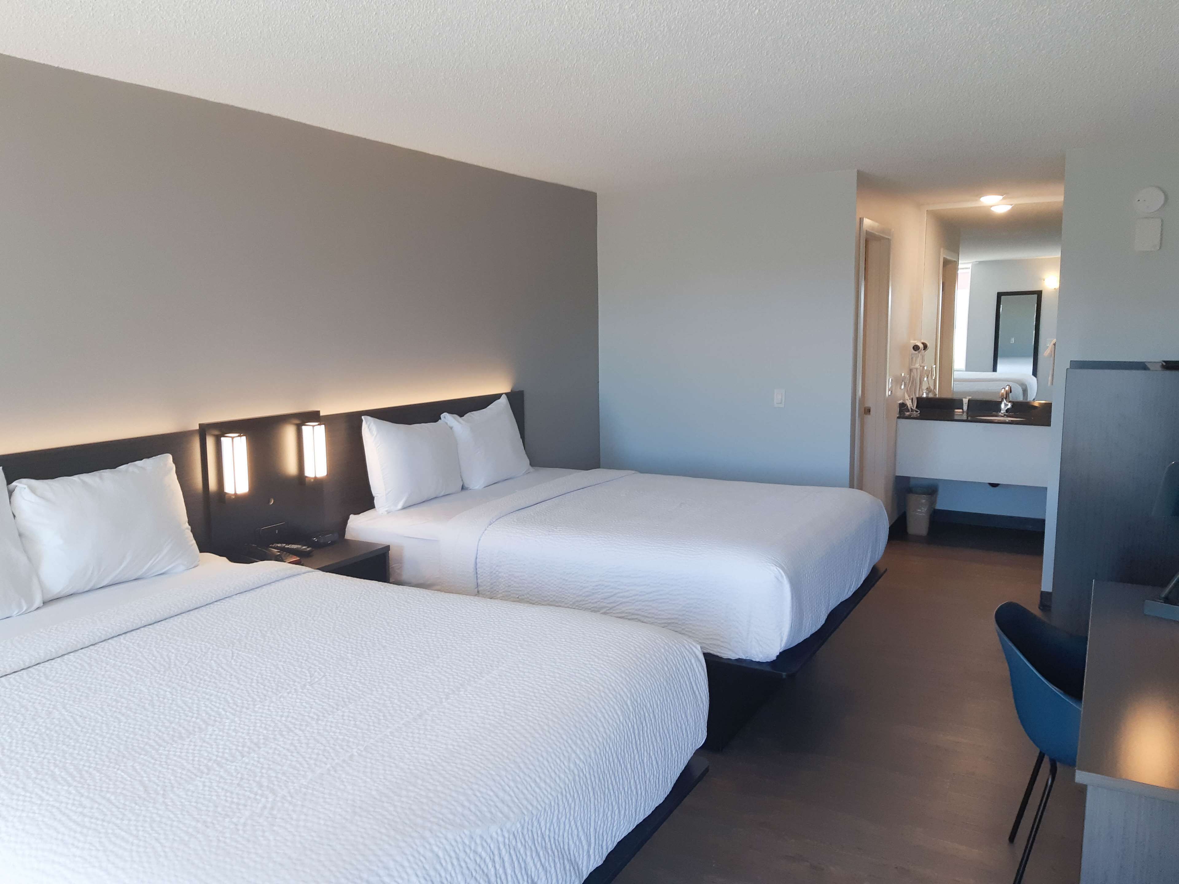 A hotel room with two beds, a desk, and a bathroom with a mirror.