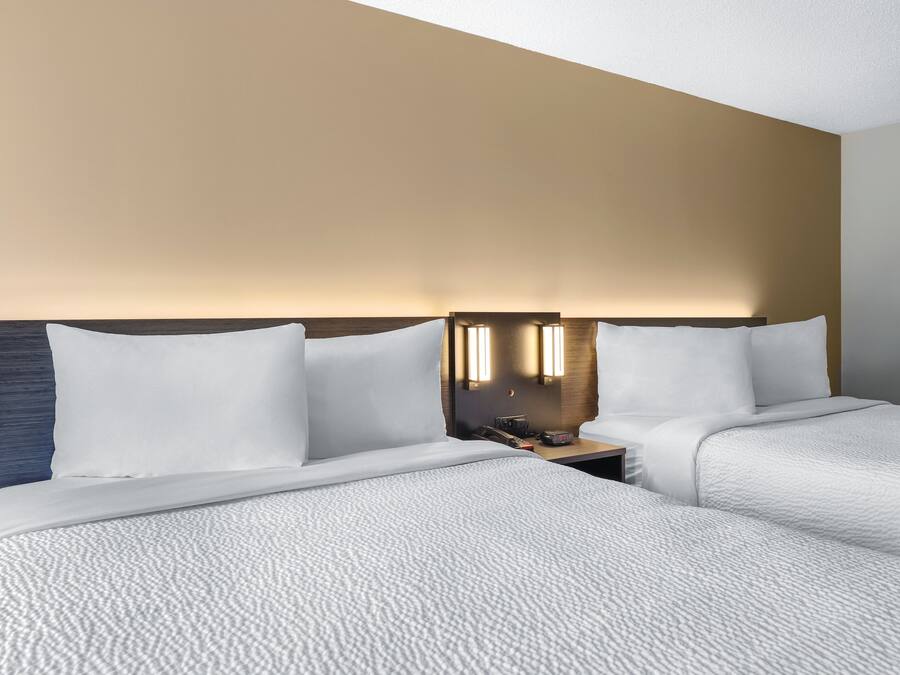 A hotel room with two beds, a nightstand, and a wall-mounted lamp.