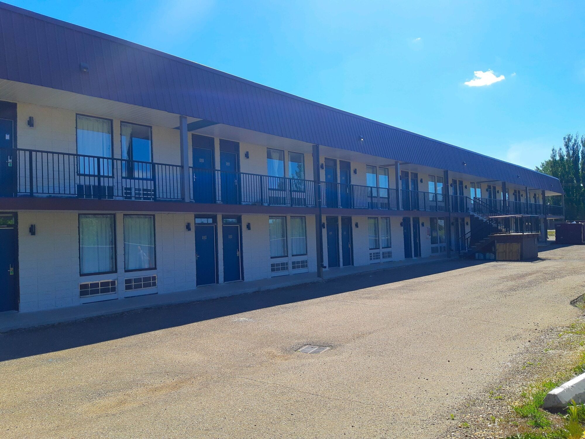 A multi-story motel with a flat roof, balconies, and a gravel parking area.