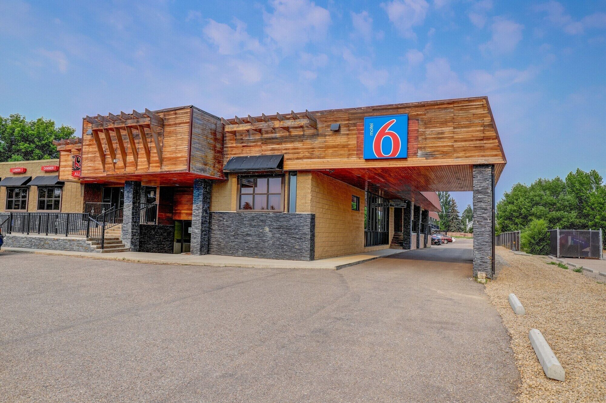 A motel with a rustic wooden facade, a prominent '6' sign, and a covered parking area.