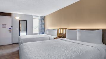 A hotel room with two beds, a nightstand, a lamp, and a window with a view.