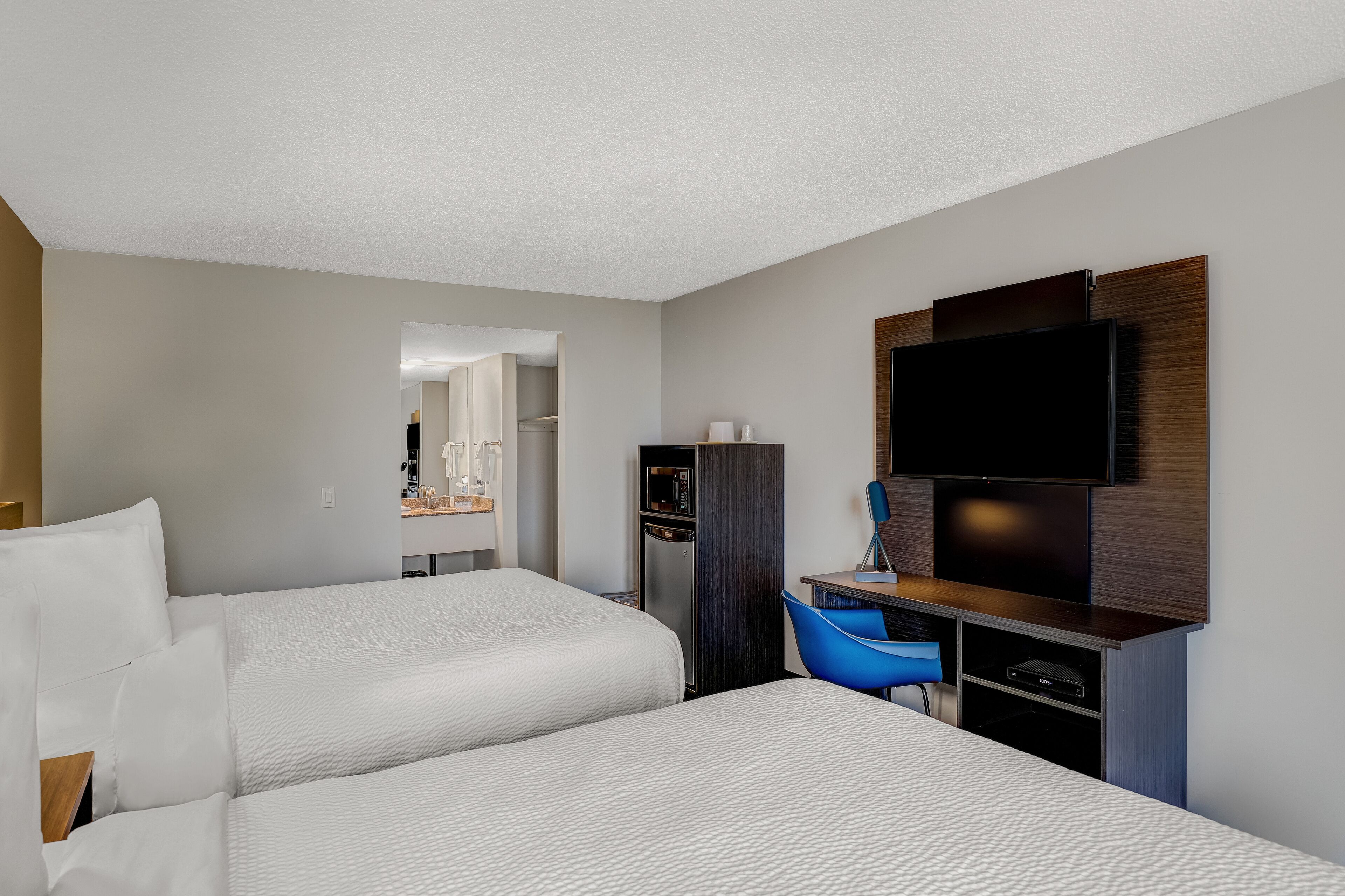 A hotel room with two beds, a TV, a desk, and a mirror.