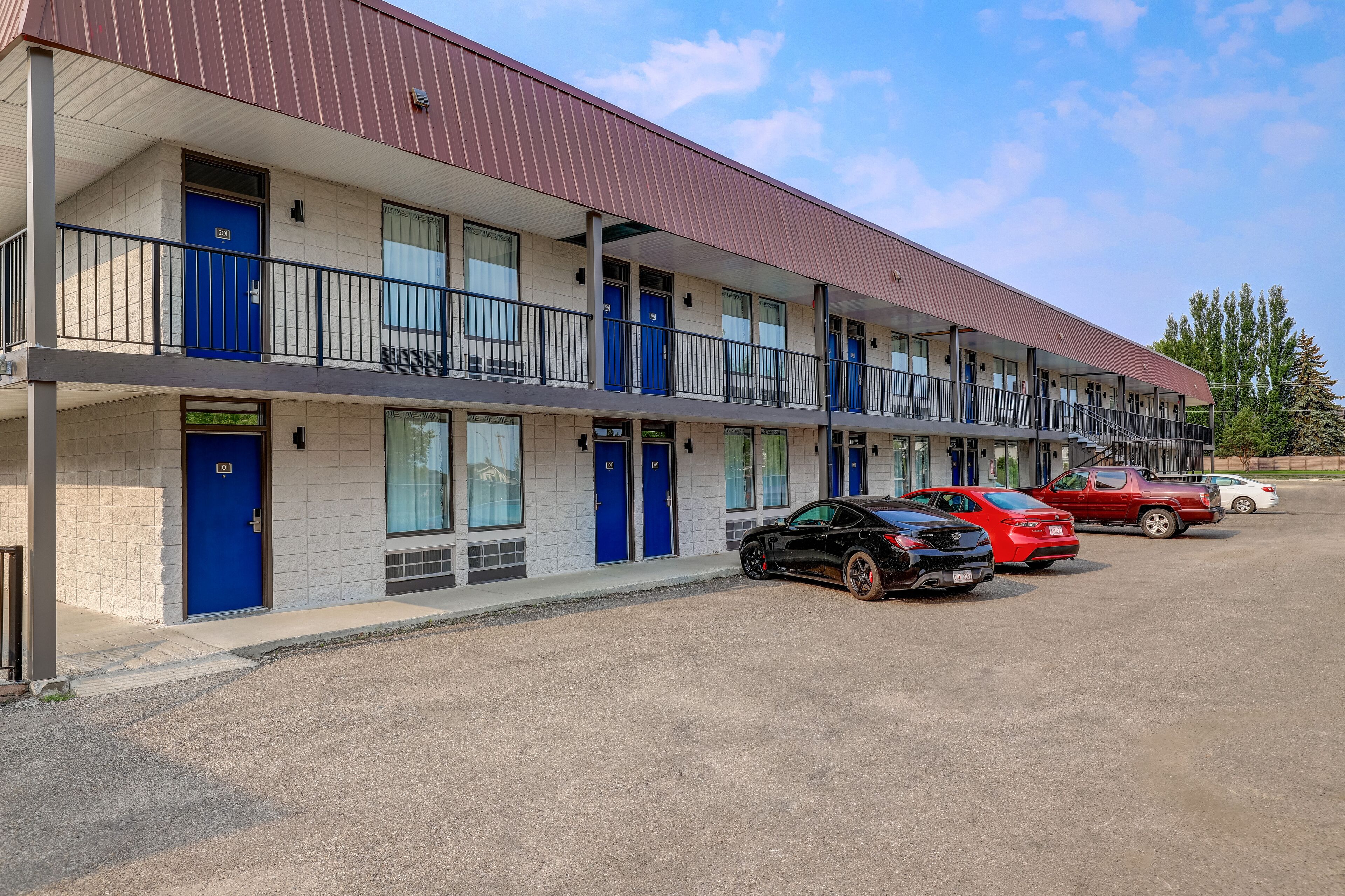 A motel with multiple floors, blue doors, and a parking area with several cars.