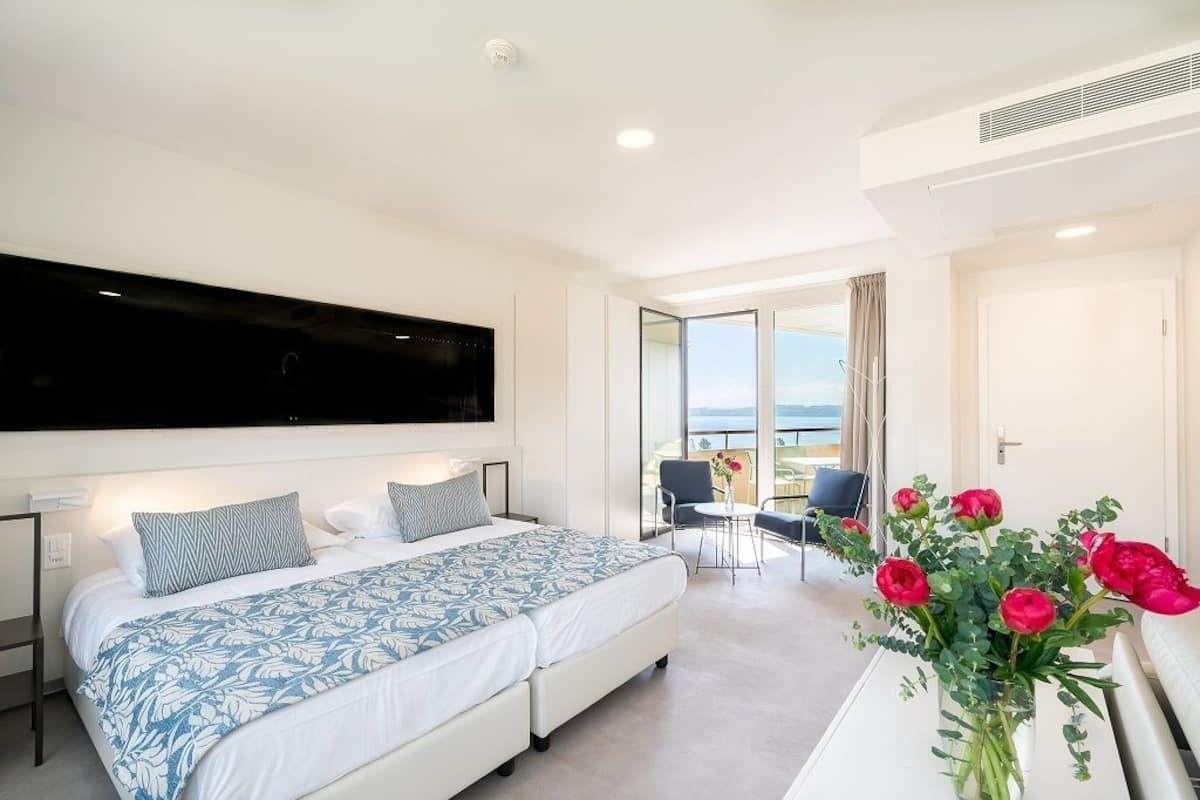 Una habitación de hotel moderna con una cama grande, un televisor de pantalla plana, un balcón con vistas y un florero con flores.