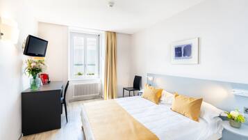 A hotel room with a bed, a desk, a chair, a TV, a window with curtains, and a wall-mounted picture.