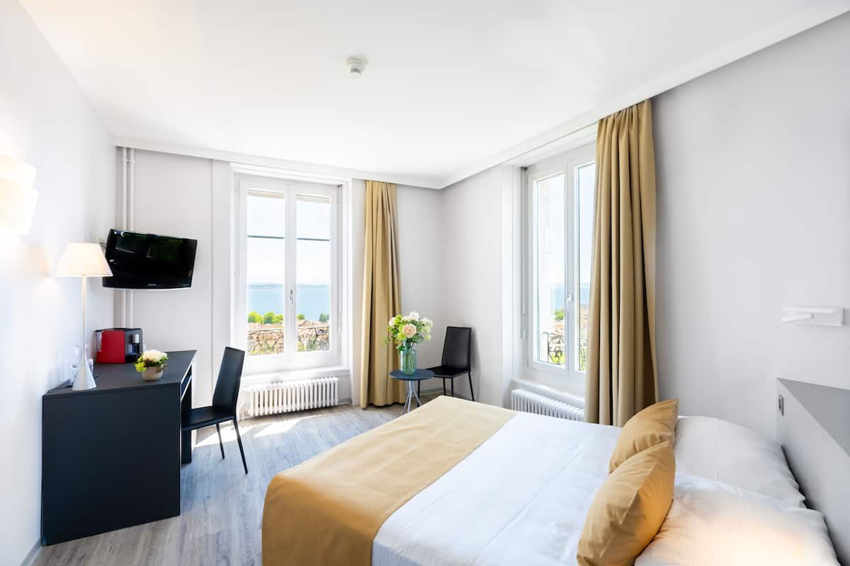 Habitación de hotel con cama, escritorio, silla, televisor y vista al exterior.