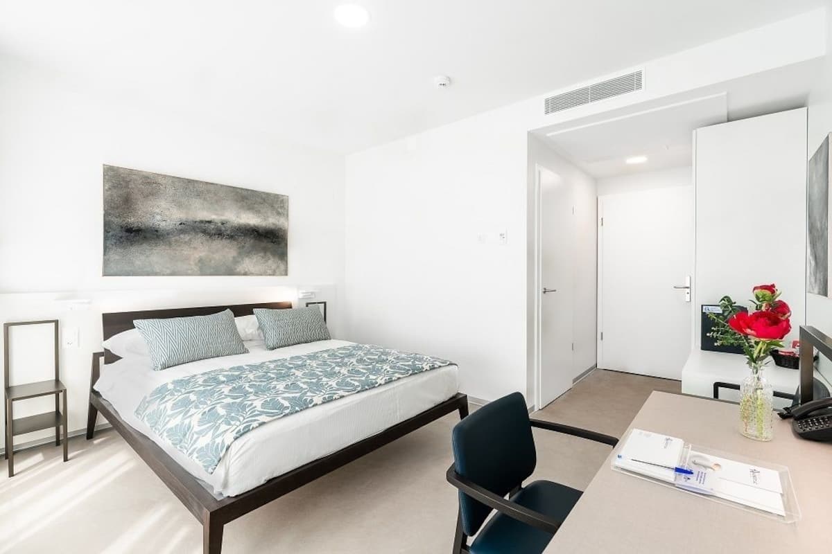 Una habitación de hotel moderna con cama, escritorio, silla y un espejo grande.