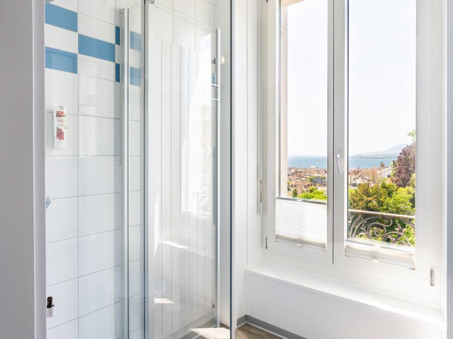 Un baño moderno con ducha de vidrio, paredes de azulejos blancos y vistas a la ciudad a través de amplios ventanales.