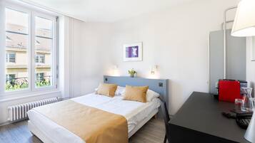 Ein Hotelzimmer mit einem Bett, einem Schreibtisch mit einem roten Telefon und einem Fenster mit Blick auf Gebäude.