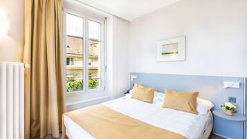 Une chambre d’hôtel avec un grand lit, une fenêtre avec des rideaux, une table de chevet avec une lampe et un tableau accroché au mur.