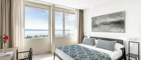 A modern hotel room with a large bed, a desk, and a view of the sea.