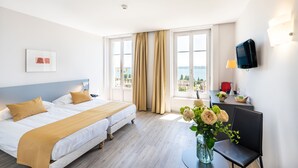 A hotel room with a bed, a desk, a chair, a TV, and a window with curtains. - Hôtel Alpes & Lac (Neuchatel)