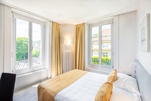 Un dormitorio con cama, dos ventanas, un radiador y vistas a zonas verdes.