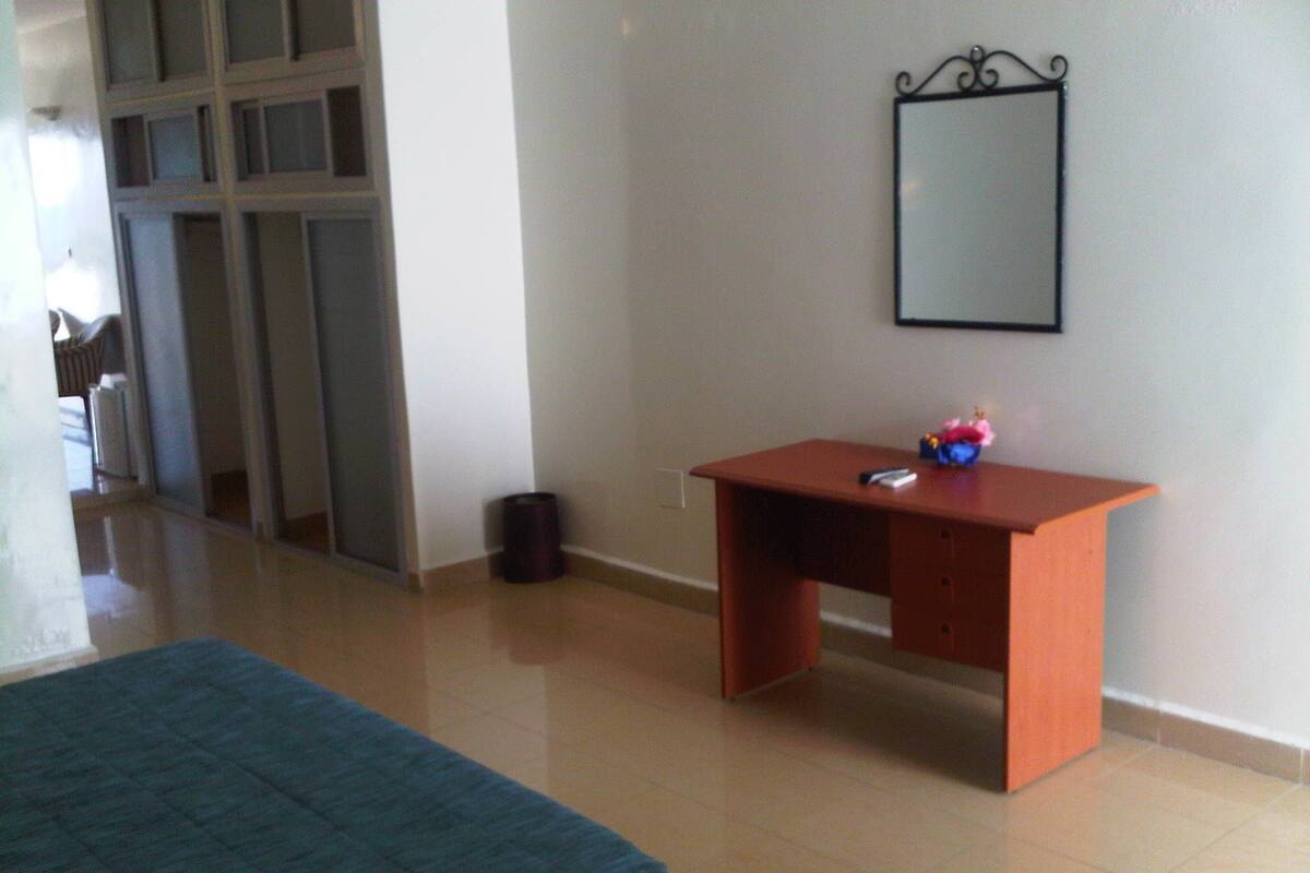 A bedroom with a bed, a desk, and a mirror.