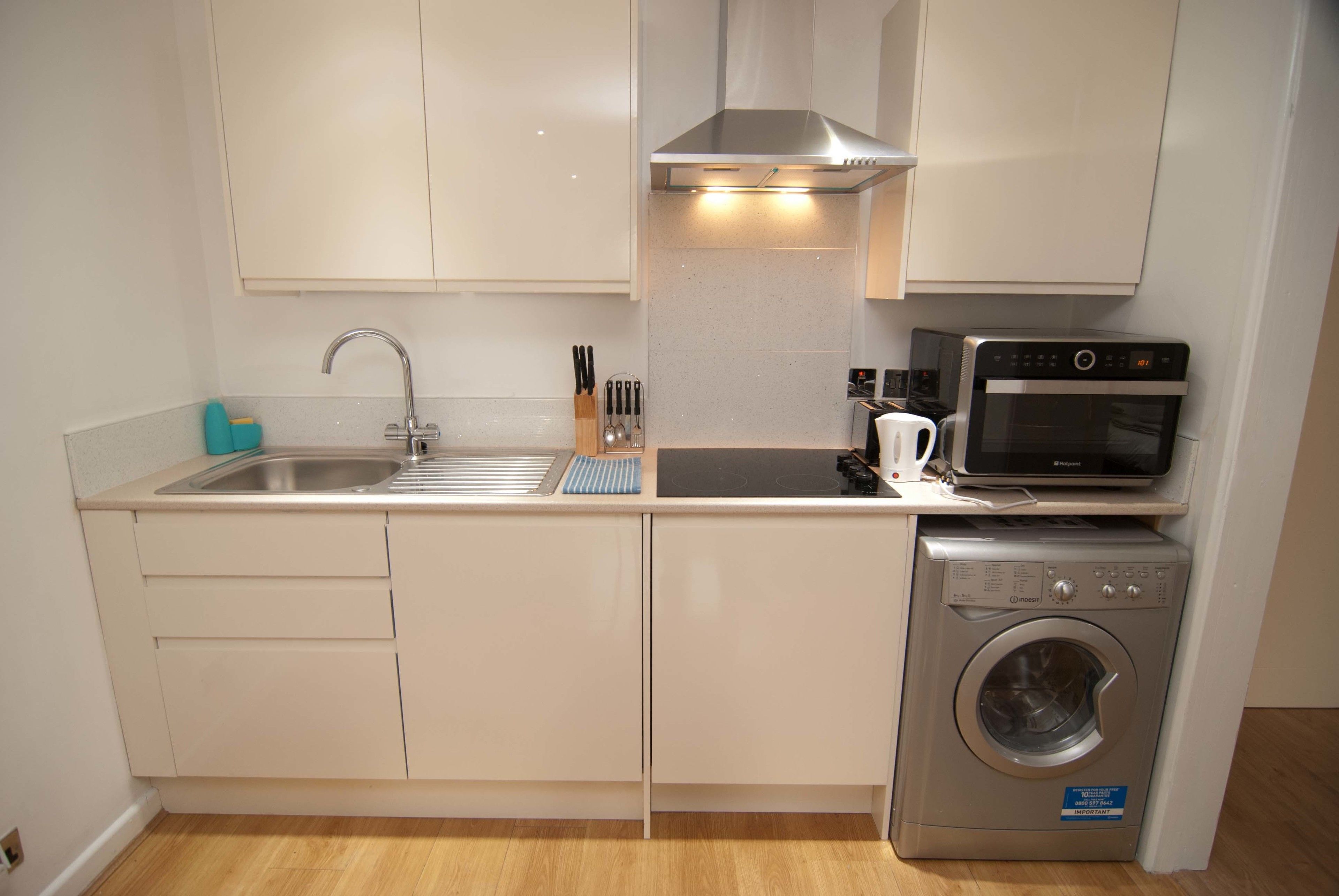 A compact kitchen with a sink, stove, microwave, and washing machine.