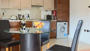 Una cocina moderna con una mesa de vidrio, un cuenco de frutas y una copa de vino.