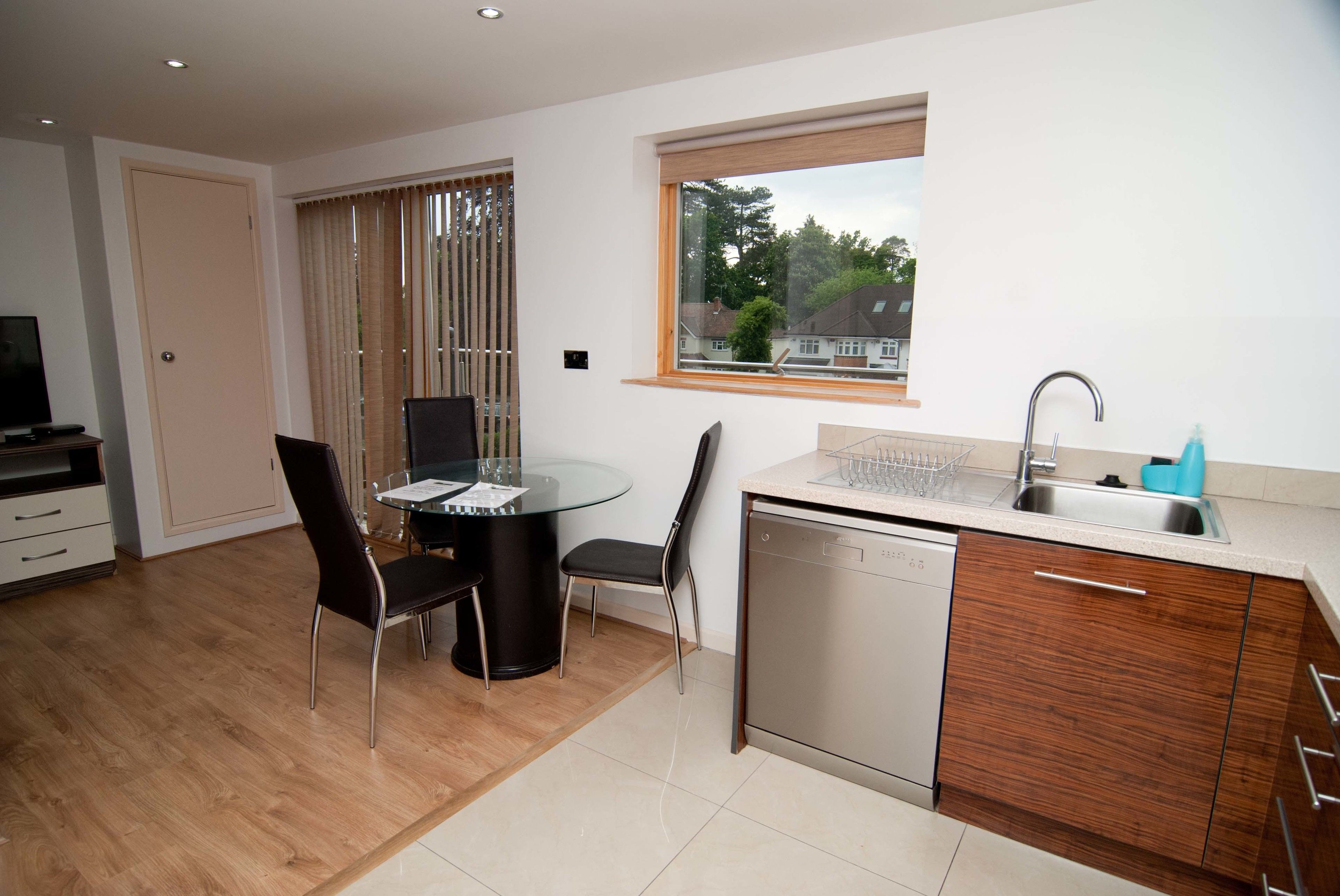A modern kitchen with a dishwasher, a sink, and a dining area with a glass table and chairs.