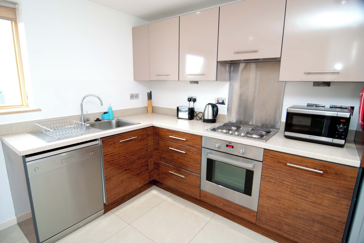A modern kitchen with a dishwasher, stove, microwave, and wooden cabinets.