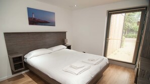 Un dormitorio con una cama grande, una mesita de noche, una lámpara de pared y un ventanal con persianas.