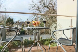 A balcony with a table and two chairs, a glass of wine, and a fruit basket. - Southampton Serviced Apartment (Southampton)