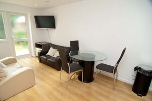 Una sala de estar moderna con una mesa de comedor de vidrio, dos sillas, un sofá y un televisor montado en la pared.