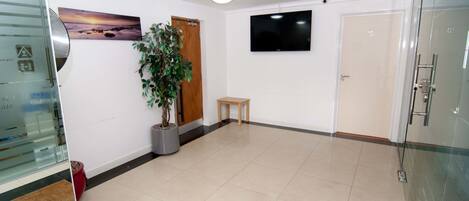 A hotel lobby with a flat-screen TV, a wooden door, a small wooden stool, and a potted plant.