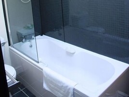 Ein modernes Badezimmer mit einer Duschkabine aus Glas, einer weißen Badewanne und einem sichtbaren WC.