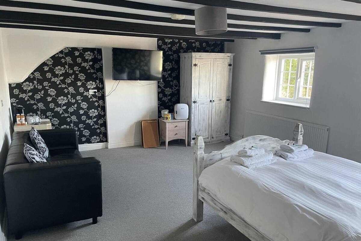 A bedroom with a bed, a desk with a chair, a wardrobe, and a TV on the wall.