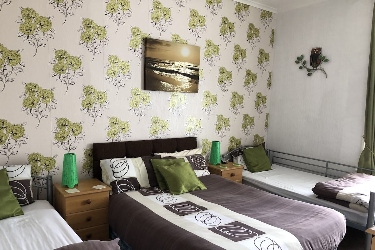 A bedroom with two beds, a nightstand, a dresser, and a wall-mounted shelf.