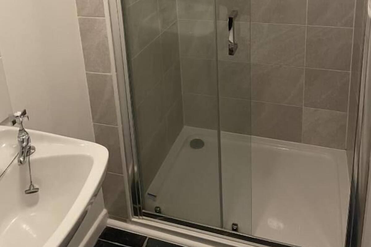 A glass-enclosed shower with a handheld showerhead and a wall-mounted faucet.
