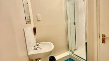 Een badkamer met een wastafel, spiegel, douche en een blauwe mat op de vloer.