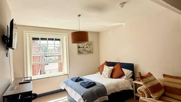 Un dormitorio con cama, escritorio, silla, ventana y lámpara de techo.