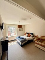 A bedroom with a bed, a desk, a chair, a window, and a ceiling light.