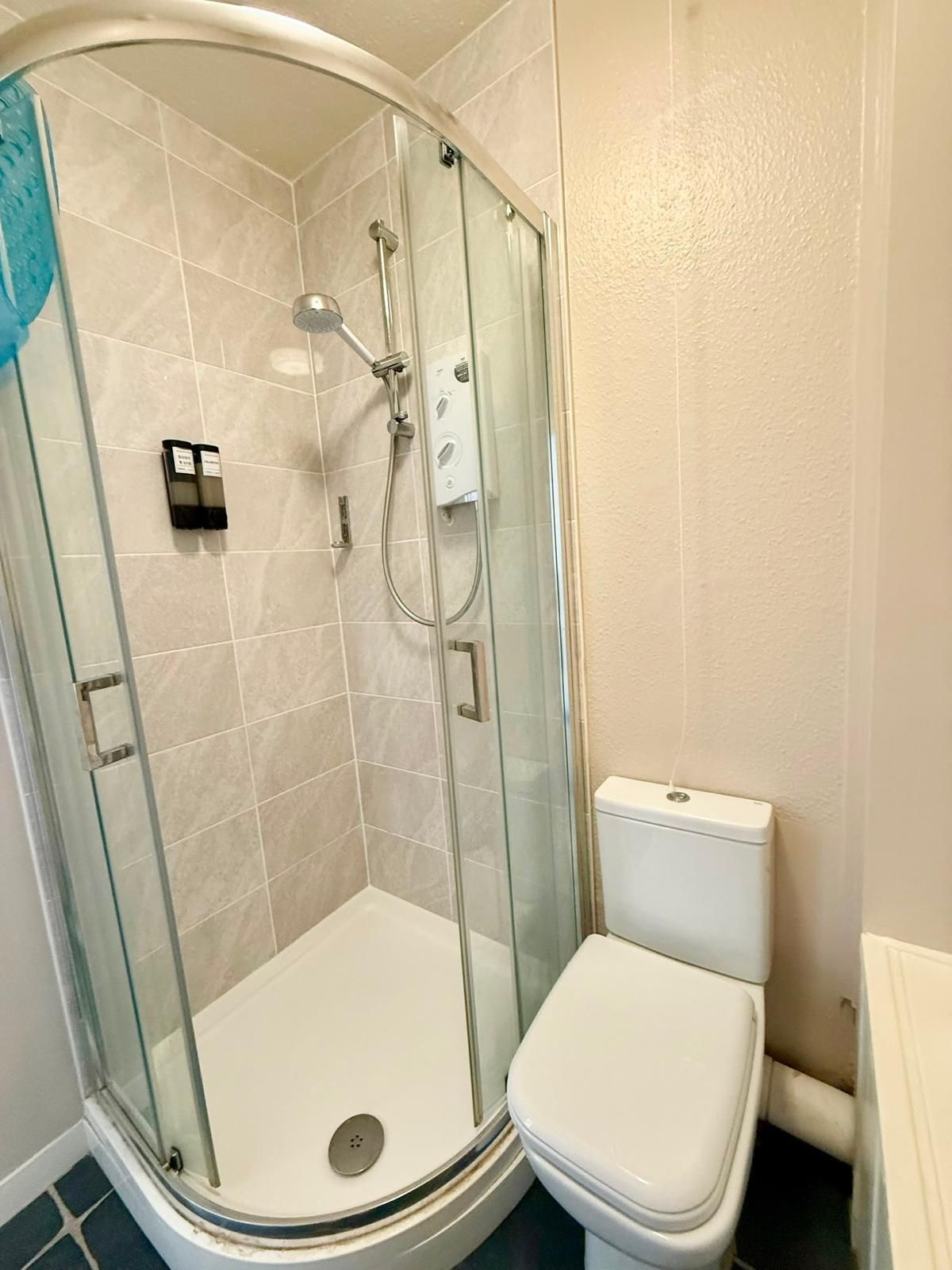Un baño con ducha de vidrio, inodoro blanco y piso de baldosas.