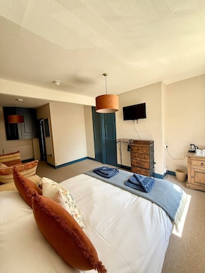 Quarto de hotel com cama, televisão de tela plana, cômoda de madeira e abajur.