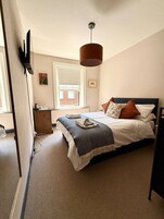 A bedroom with a bed, a dresser, a radiator, a window, and a hanging lamp.