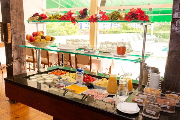 A buffet with various food items and beverages, including fruits, cheeses, and a juice dispenser. - VOA Hotel União (Caxambu)