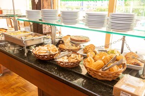 A buffet with various food items and stacked plates on a glass display. - VOA Hotel União (Caxambu)
